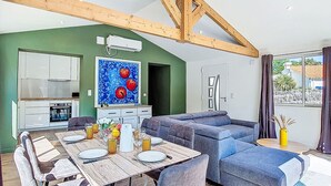 Ett modernt vardagsrum med ett träpanelat tak, en matplats med ett bord för fyra personer och ett kök i bakgrunden.