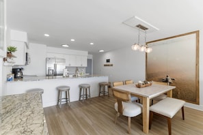 Cozinha moderna com armários brancos, ilha central, banquetas e mesa de jantar com cadeiras.