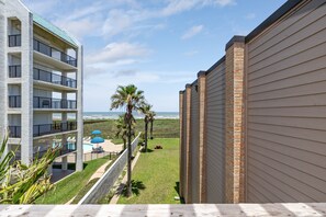 A multi-story building with balconies, a pool area with umbrellas, and a view of the ocean.