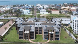 A multi-story hotel with a central courtyard, surrounded by a parking lot and palm trees. - 2-Bedroom Beachfront Comfort w/ Heated Pool! (South Padre Island)