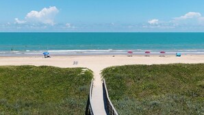 A beach with a wooden walkway leading to the shore, surrounded by greenery. - 2-Bedroom Beachfront Comfort w/ Heated Pool! (South Padre Island)