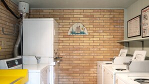 A laundry room with a brick wall, a mural of sailboats, and multiple washing machines. - 2-Bedroom Beachfront Comfort w/ Heated Pool! (South Padre Island)