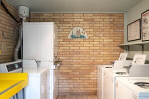 A laundry room with a brick wall, a mural of sailboats, and multiple washing machines.