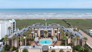 A hotel with a central pool, surrounded by palm trees and a view of the beach and ocean. - 2-Bedroom Beachfront Comfort w/ Heated Pool! (South Padre Island)