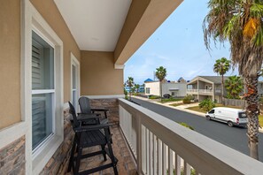 A balcony with a stone wall, a black chair, and a white van parked on the street. - Beautiful Coastal Sol Villa • Heated Pool • 3 Min Walk to Beach (South Padre Island)