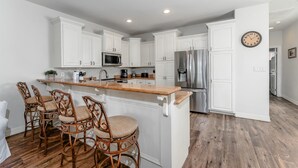 A modern kitchen with white cabinetry, a central island with bar stools, stainless steel appliances, and a clock on the wall. - Beautiful Coastal Sol Villa • Heated Pool • 3 Min Walk to Beach (South Padre Island)