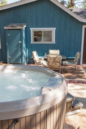 Un bain à remous dans un jardin, avec un abri bleu, une fenêtre et du mobilier d’extérieur.