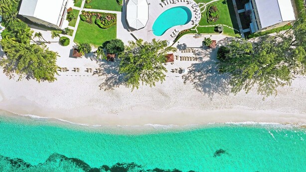 Ein Luftbild eines Resorts mit Schwimmbad, Strand und klarem türkisblauem Wasser.