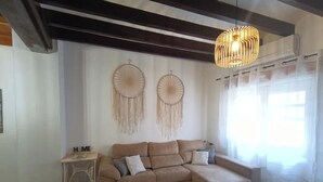 Een woonkamer met een beige modulaire bank, een klein bijzettafeltje, twee wanddecoraties van droomvangers, en een hanglamp.