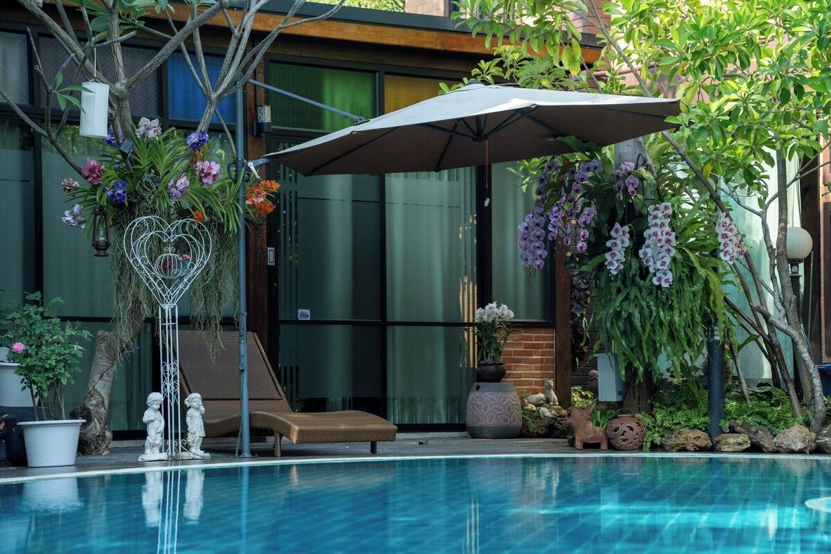 Et poolområde med liggestol, parasol og dekorative planter.