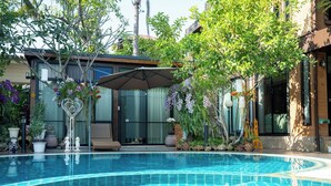 Une piscine dont le bord est revêtu de carreaux, entourée de plantes en pot et de mobilier d’extérieur.