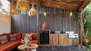 Una terraza de madera con sofá integrado, un refrigerador pequeño y una parrilla.