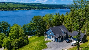 A house with a large garage, a driveway, and a view of a lake. - NEW Build Keuka Lakefront | Sleeps 16 | Dock/Kayak (Penn Yan)