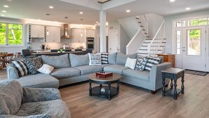 A spacious living room with a grey sectional sofa, a coffee table, and a staircase leading to an upper level. - NEW Build Keuka Lakefront | Sleeps 16 | Dock/Kayak (Penn Yan)