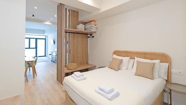 Ett modernt hotellrum med en stor säng, ett träbeklätt sänggavel och en inbyggd hylla med handdukar.