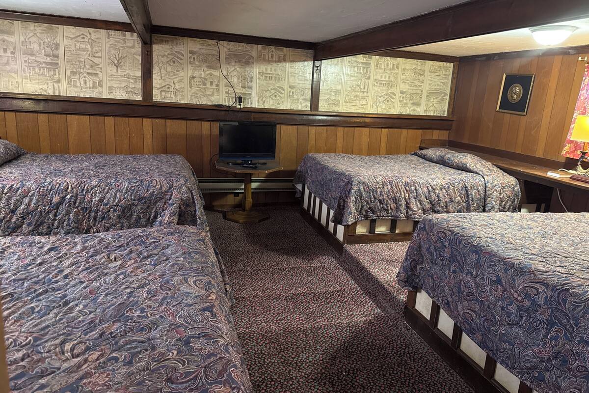 A room with four beds, a television, and a patterned wallpaper.