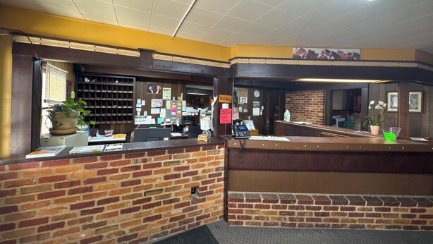 A reception area with a brick wall, a reception desk, a computer, a phone, and a plant. - plains motel  (Douglas)
