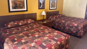 A hotel room with two beds, each with a floral-patterned quilt, a nightstand with a lamp, and three framed pictures on the wall. - plains motel  (Douglas)