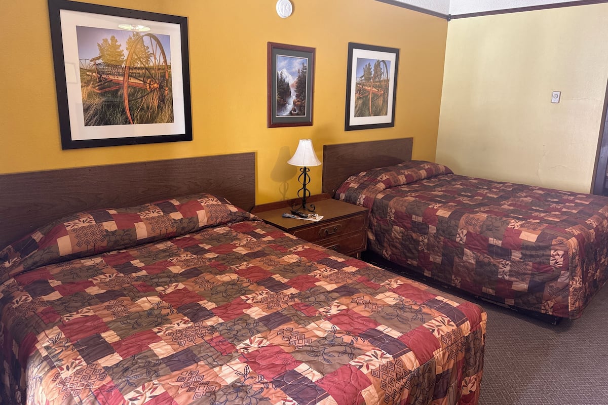 A hotel room with two beds, each with a floral-patterned quilt, a nightstand with a lamp, and three framed pictures on the wall.