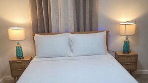 A neatly made bed with white linens, two bedside tables with lamps, and a window with curtains.