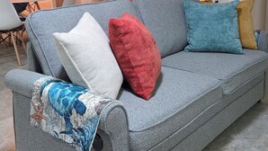 A grey sofa with multiple cushions, a hanging light fixture, and two wall-mounted artworks.