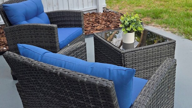 An outdoor wicker sofa with blue cushions, a small table, and a potted plant.