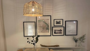 Un coin repas avec une table en bois, des chaises, un luminaire suspendu en fibres tressées et des tableaux encadrés accrochés au mur.