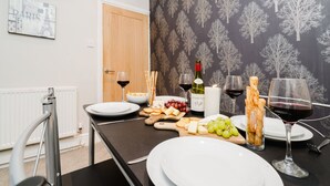 A dining area with a table set for two, featuring a bottle of wine, glasses, cheese, crackers, and grapes. - Cosy 4-Bed - Sleeps 7, Garden (Birmingham)