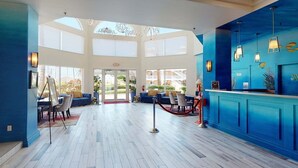 Un hall d’entrée spacieux avec un plafond haut, un comptoir de réception et un espace salon agrémenté d’un mur bleu et offrant une vue sur l’extérieur.