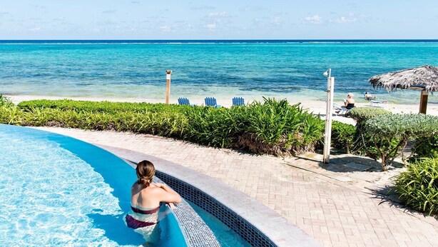 Un espace aménagé au bord de la piscine, offrant une vue dégagée sur l’océan, avec une structure recouverte de chaume et un chemin pavé.