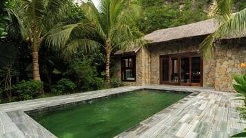 Una casa de piedra con techo de paja, piscina y exuberante vegetación tropical.