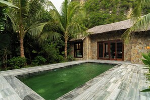 A stone house with a thatched roof, a swimming pool, and lush tropical vegetation. - Bliss Tam Coc Resort Ninh Binh (Nam Hoa Lu)