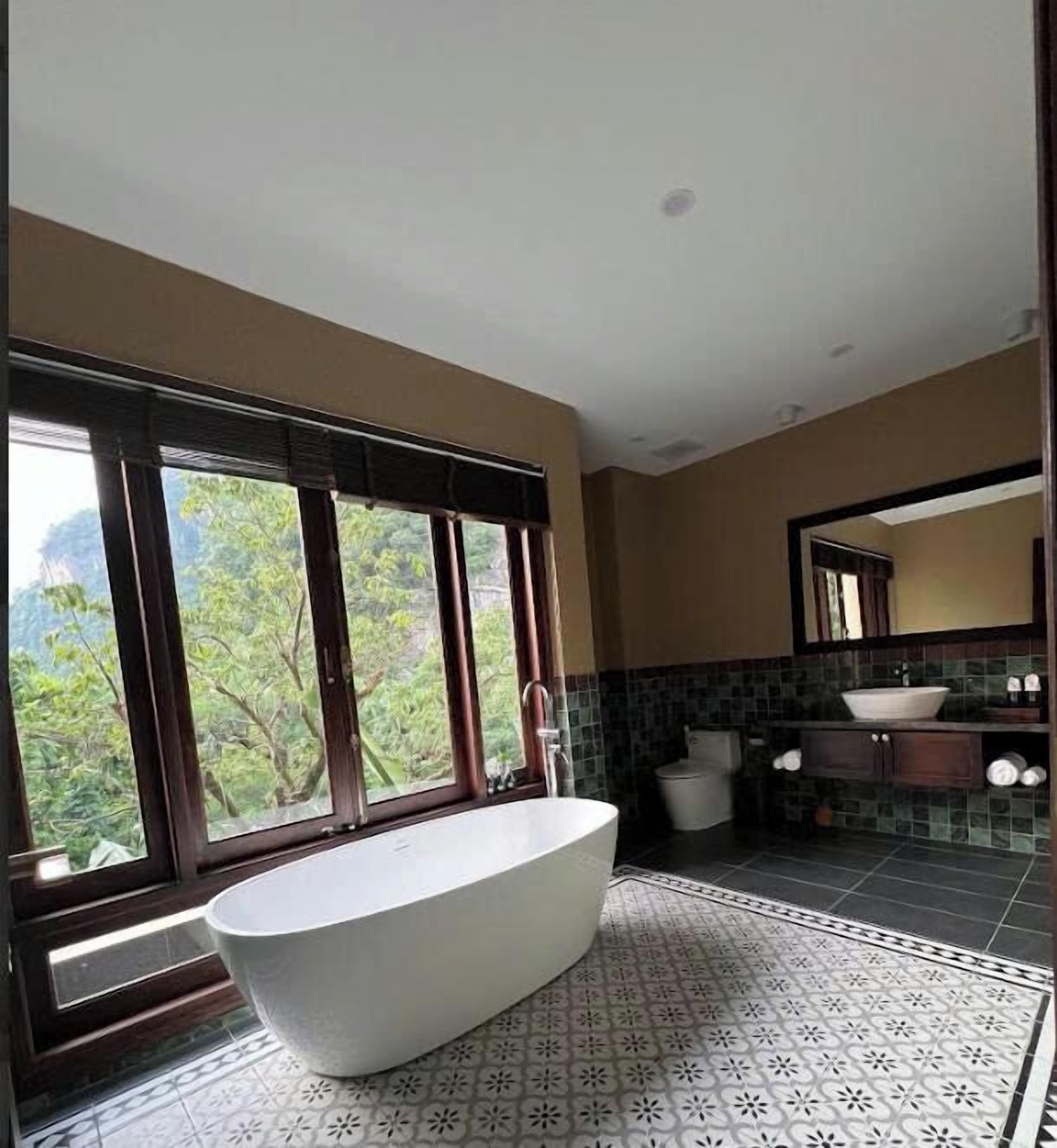 Un bagno moderno con una vasca freestanding, ampie finestre, un pannello di piastrelle e uno specchio sopra il lavabo.