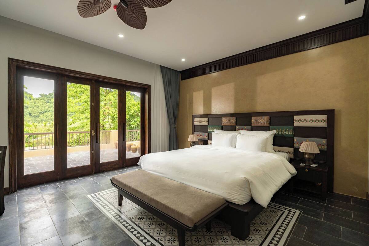 Un dormitorio amplio con una cama grande, un banco y vistas al exterior por una puerta corrediza de vidrio.