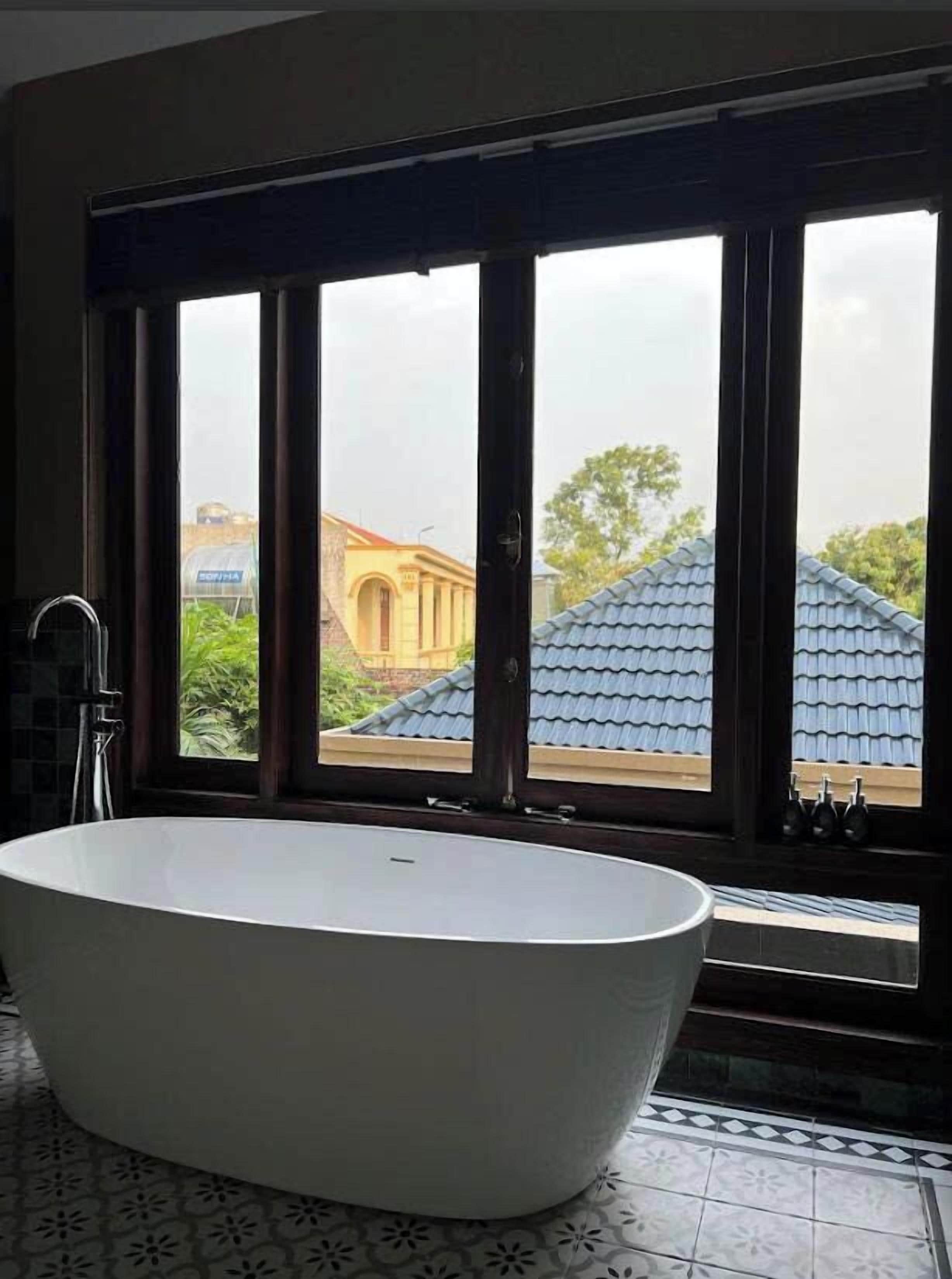 A bathroom with a freestanding bathtub, large windows, and a view of buildings and trees.