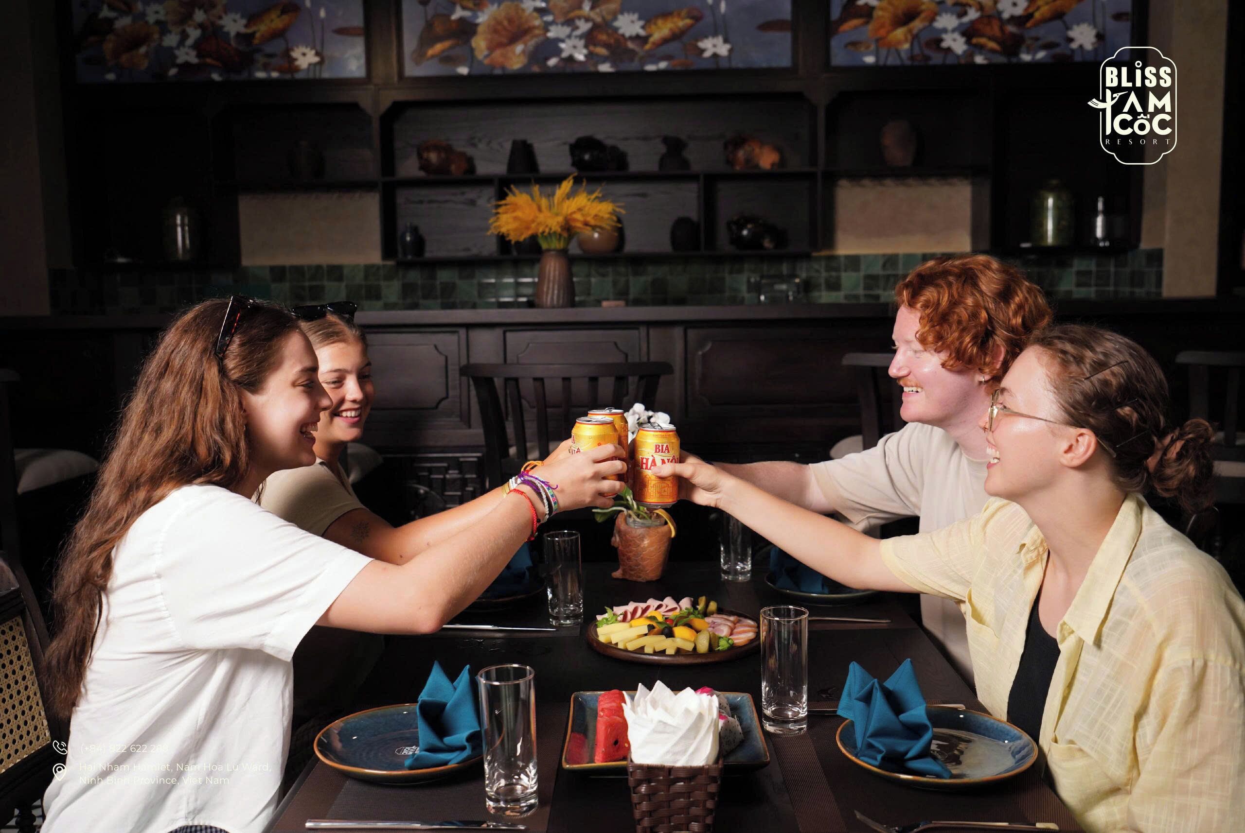 Un grupo de personas brindando con bebidas en una mesa con un centro de mesa floral y un plato de fruta.