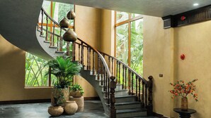 Una escalera con balaustres de madera y un diseño curvo que conduce a un rellano con plantas en macetas y un jarrón de flores.