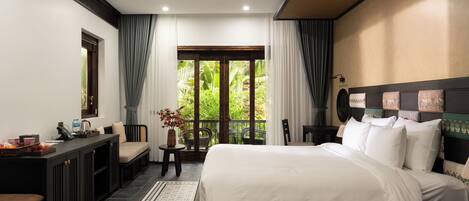 A bedroom with a large bed, a desk, and a chair. There is a window with curtains and a view of greenery outside.