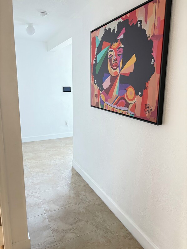 A hallway with a colorful abstract painting on the wall, a white door, and a tiled floor.