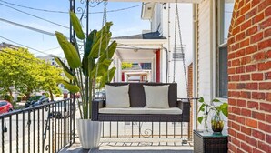 A balcony with a wicker sofa, a potted plant, and a hanging chair.