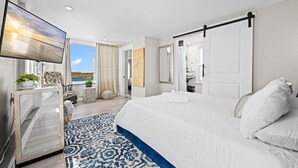 Une chambre moderne avec un grand lit, une télévision, un balcon avec vue et une salle de bain avec un miroir.