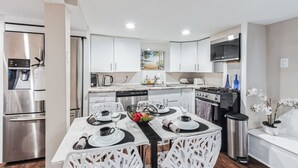 Een moderne keuken met witte kasten, roestvrijstalen apparatuur en een eethoek met een tafel voor twee.