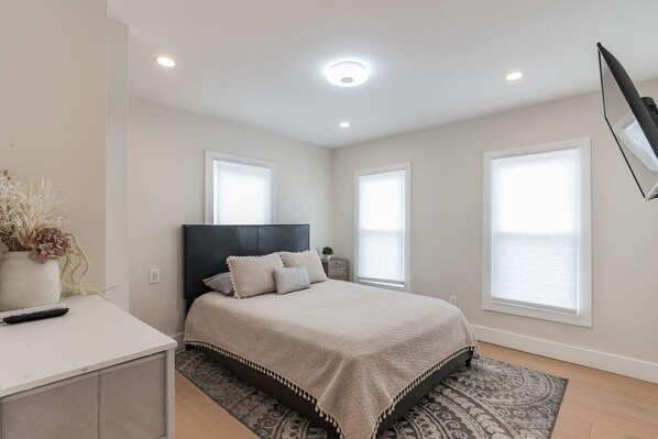 A bedroom with a bed, bedside tables, a nightstand, a window, and a ceiling light.