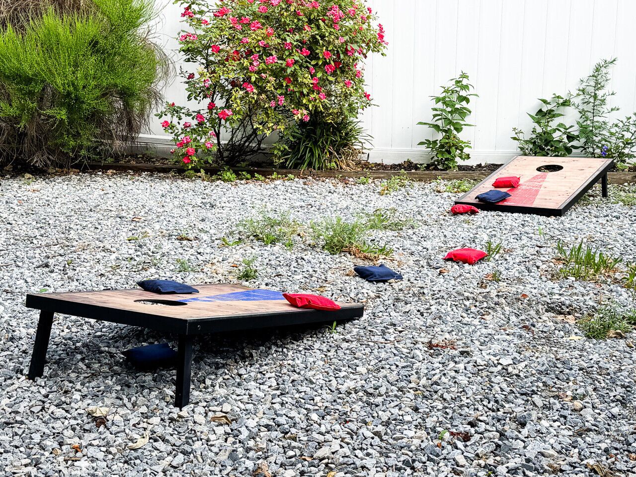 Un jardín con una mesa de juegos de madera y una pequeña maceta con flores rosas.