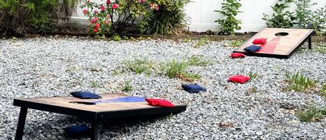 Un jardín con una mesa de juegos de madera y una pequeña maceta con flores rosas.
