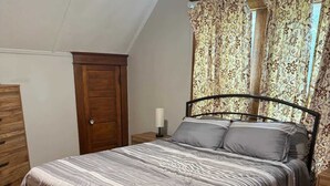 A bedroom with a bed, wooden wardrobe, and a window with floral curtains. - The Spruce House  Family 4BR 2 Bath, Great Location, In Ogallala, Close to Lake McConaughy (Ogallala)