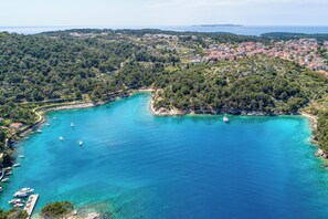 Luchtbeeld van een kustplaatsje met een baai, boten en weelderige begroeiing.