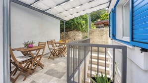 Eine überdachte Terrasse mit Holzmöbeln, einer Steinmauer und einer blauen Tür.
