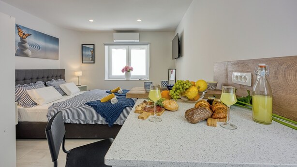 Ein modernes Schlafzimmer mit Bett, Nachttisch und Frühstücksecke mit Brot, Obst und Getränken.