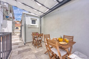 A balcony with a table set for breakfast, including bread, pastries, and juice.